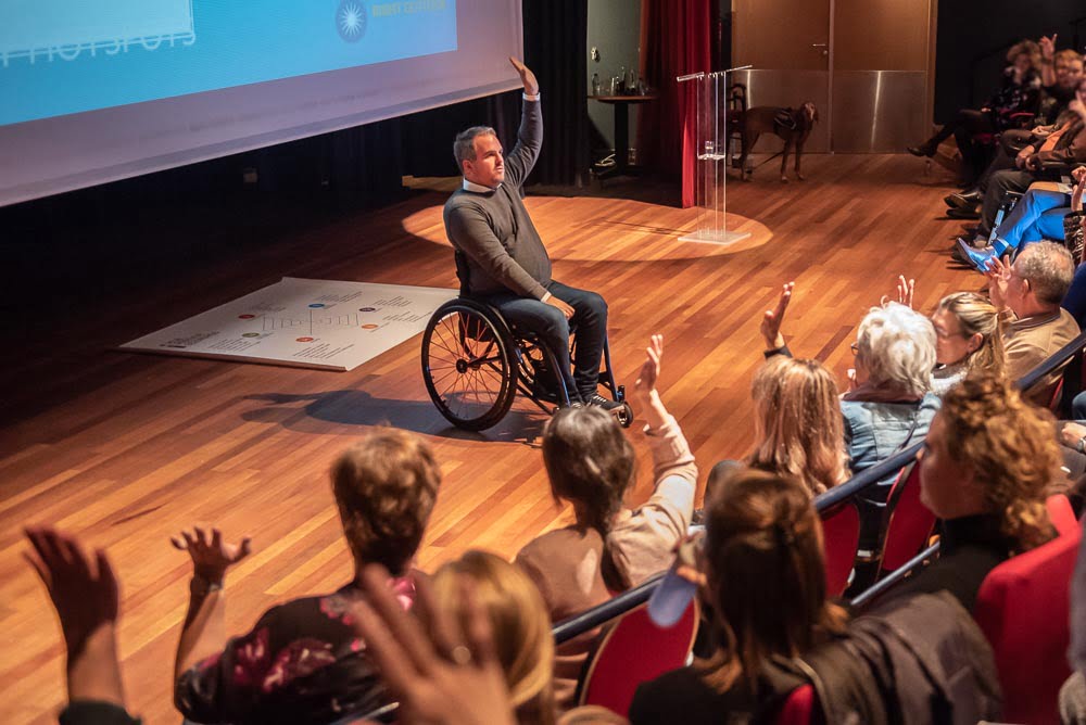 Niek van den Adel op podium met zorgmedewerkers als publiek